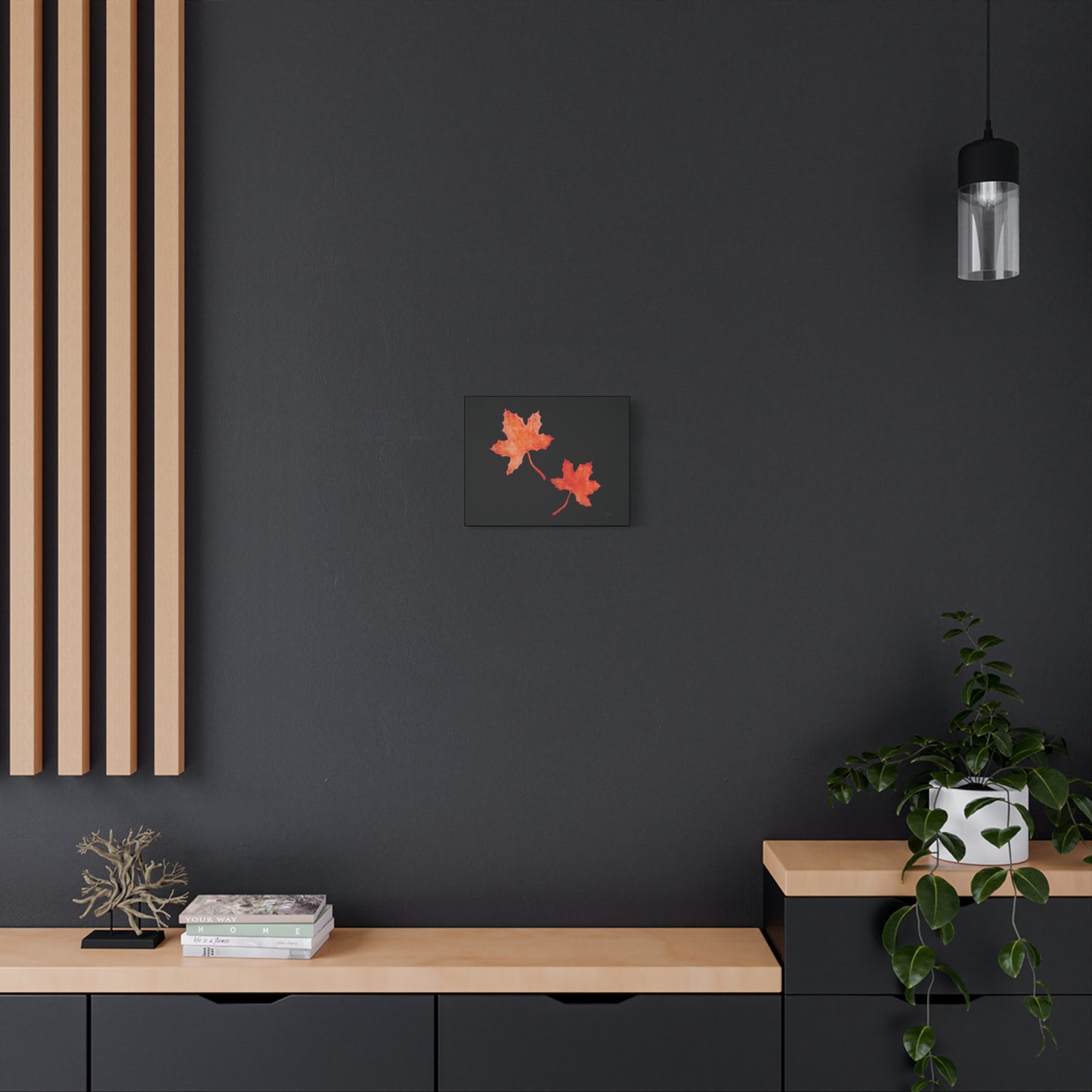 14" x 11" black stretched canvas with two watercolour hand-painted orangey-red maple leaves and eKuumeArt logo - displayed on dark modern wall with wooden countertop dresser/nook and decor