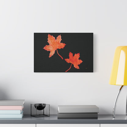 18x12" Black stretched canvas print with two orange-red watercolour maple leaves and eKuumeArt logo – displayed on wall above a decorated grey countertop dresser.