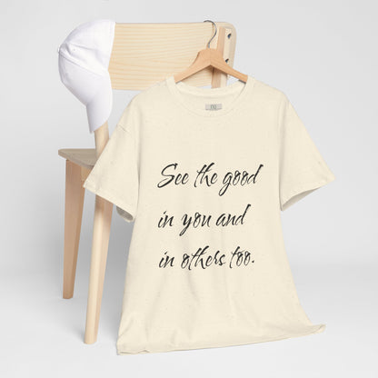 Natural/beige t-shirt with motivational quote text on a wooden hanger - hanging on wooden chair backing with a white cap on it.