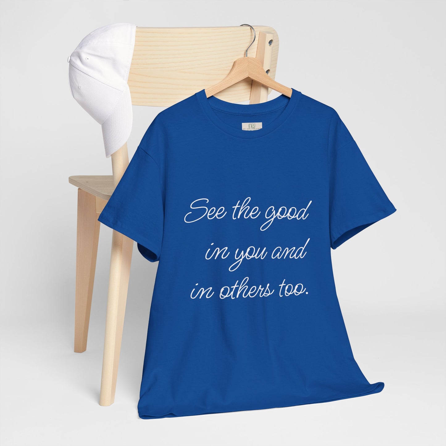 Royal Blue t-shirt with motivational quote text on a wooden hanger - hanging on wooden chair backing with a white cap on it.