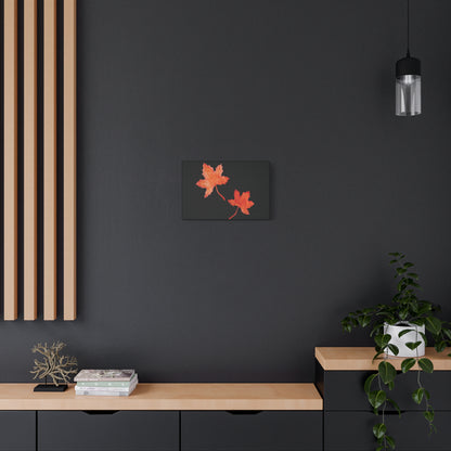 18x12" Black stretched canvas with two orange-red watercolour maple leaves and eKuumeArt logo – displayed on dark modern wall above a decorated wooden countertop dresser.