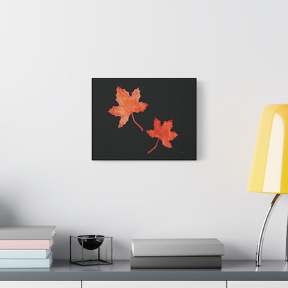 14x11" Black stretched canvas print with two orange-red watercolour maple leaves and eKuumeArt logo – displayed on wall above a decorated grey countertop dresser.