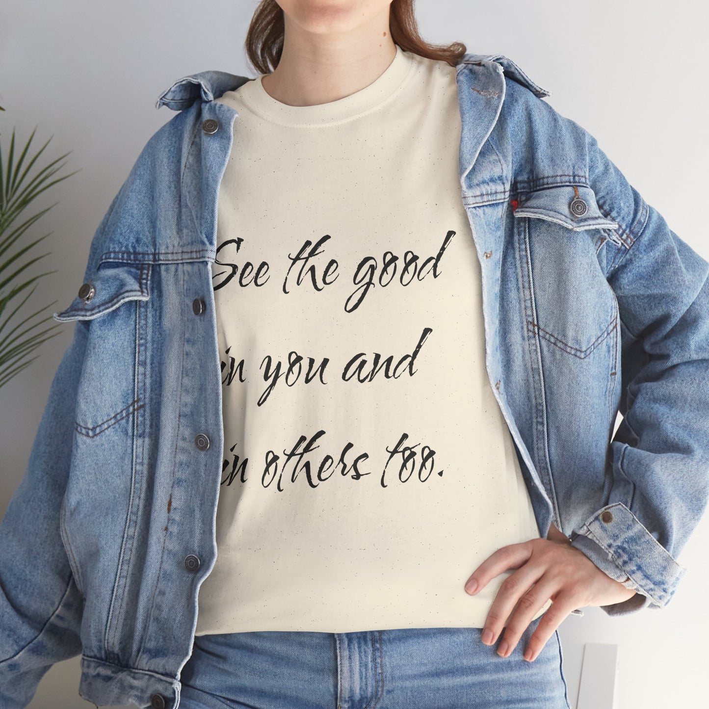 Woman wearing a natural/beige heavy cotton t-shirt with motivational quote text, styled with a denim jacket - closeup view.