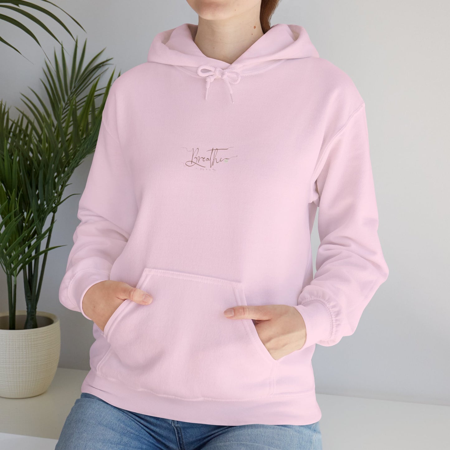 Woman wearing light pink hoodie - closeup of 'Breathe' handwritten text on chest, also featuring a palm plant in the background