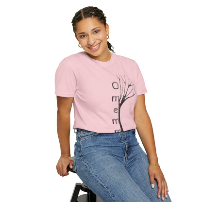 Woman seated on stool wearing blossom tshirt with hand-drawn tree, 'Omemma' text and eKuumeArt logo on torso.