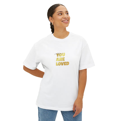 Woman wearing white oversized boxy t-shirt adorned with 'You Are Loved' text in gold on chest.
