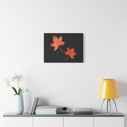 24x18" Black stretched canvas print with two orange-red watercolour maple leaves and eKuumeArt logo – displayed on wall above a decorated grey countertop dresser.