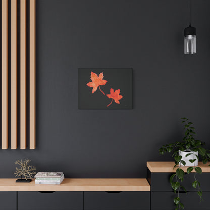 24x18" Black stretched canvas with two orange-red watercolour maple leaves and eKuumeArt logo – displayed on dark modern wall above a decorated wooden countertop dresser.