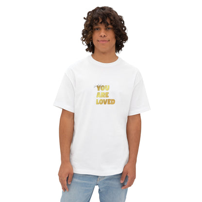 Man wearing white oversized boxy t-shirt adorned with 'You Are Loved' text in gold on chest.