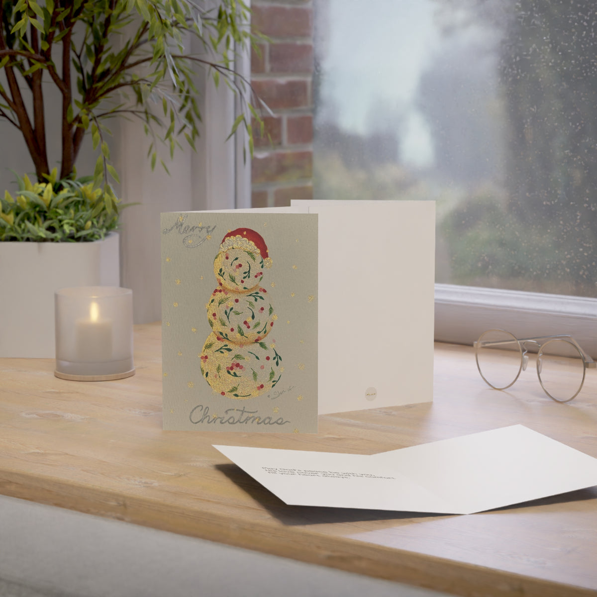 Christmas holiday card adorned with handmade painting of a vintage snowman, on a wooden surface near a window with a warm setting – 5"x7" front, back and inside covers | Eku ume Hope | Art.