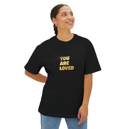 Woman wearing black oversized boxy t-shirt adorned with 'You Are Loved' text in gold on chest.