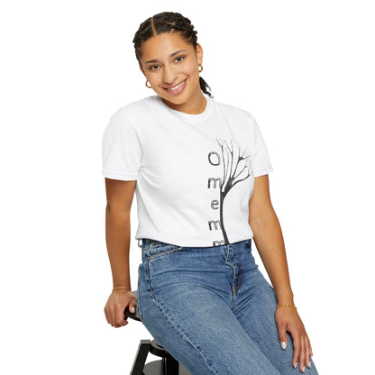 Woman seated on stool wearing white tshirt with hand-drawn tree, 'Omemma' text and eKuumeArt logo on torso – tucked in pants.