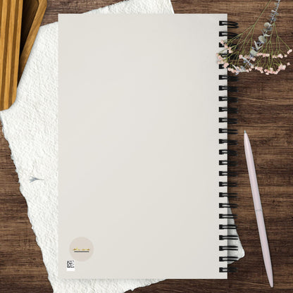 Spiral journal/notebook with ekuumeArt logo on the back cover – displayed on a wooden surface with a pen, textured paper, a flower and wooden box.