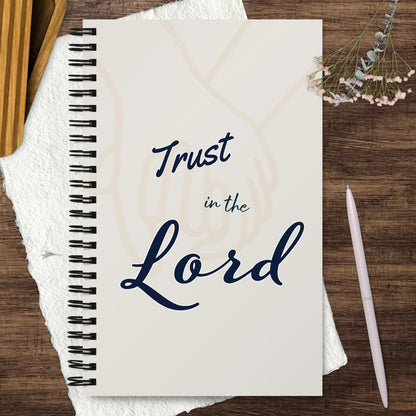 Spiral journal/notebook with 'Trust in the Lord' text on the cover – displayed on a wooden surface with a pen, textured paper, a flower and wooden box around it.