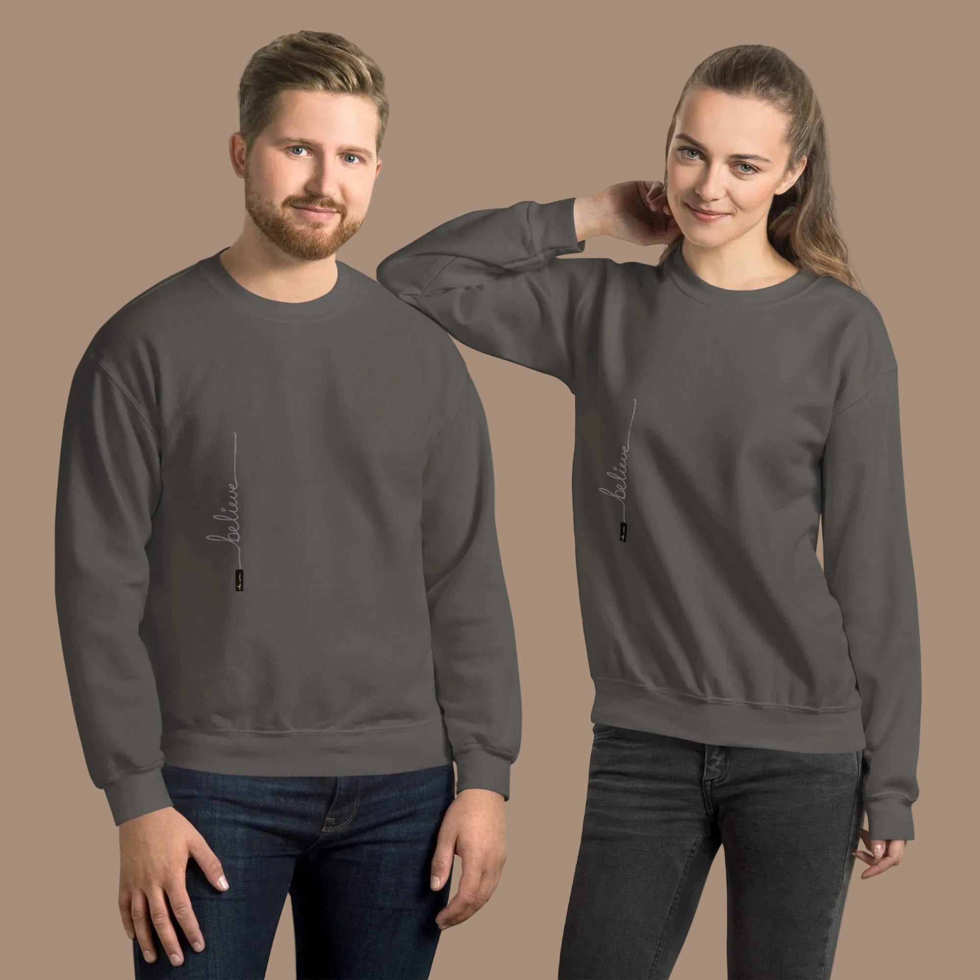 Man and woman wearing charcoal sweaters with 'Believe' handwritten text and eKuumeArt logo on torso – front view.