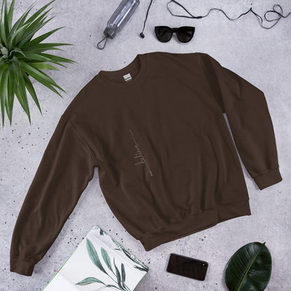 Dark Chocolate sweater with 'Believe' handwritten text and eKuumeArt logo on torso – featured on a stone surface with plant, journal and other daily items around it.