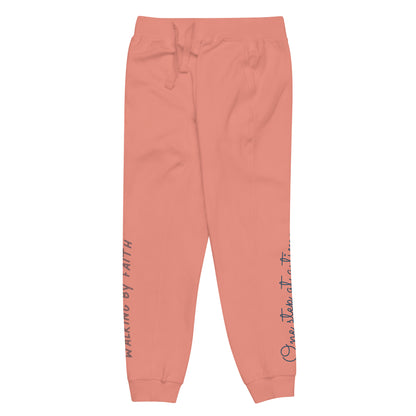 Dusty rose sweatpants adorned with 'Walking by faith' text and eKuumeArt logo on front right leg and glimpse of 'One step at a time' on back left leg – side view.