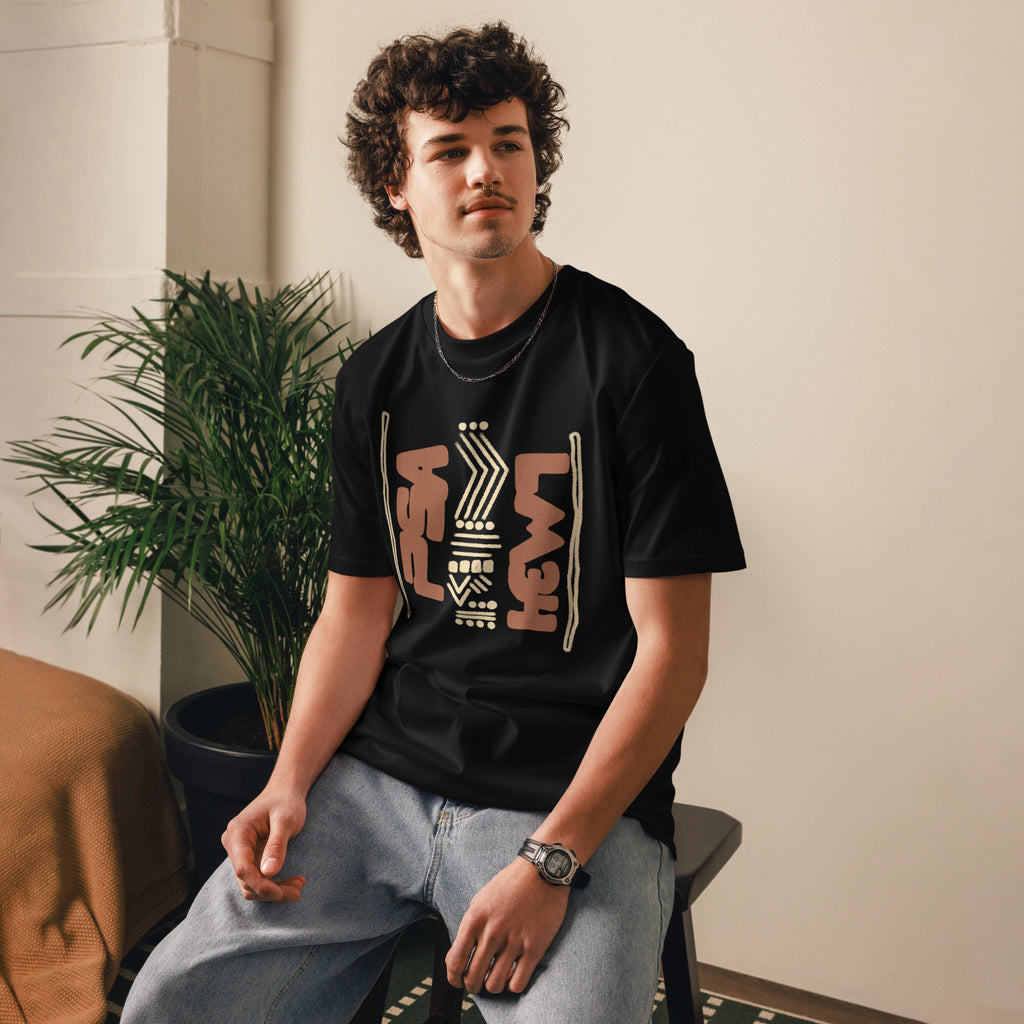 Man wearing a black organic cotton t-shirt with hand-drawn design, sitting on a stool in a calm room setting | eKuumeArt.