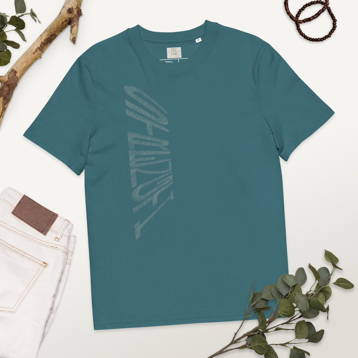 Stargazer blue organic cotton t-shirt with hand-drawn 'Strength' text and white jeans on a white surface with greenery | eKuumeArt.